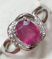 Close-up photo of silver ring with oval red ruby and small clear stones on a polished silver band.