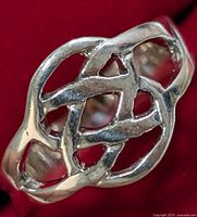 Close-up photo of silver ring showing the intricate Celtic knot openwork design on a red background.