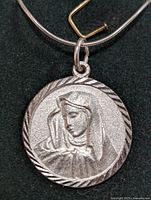 Front view of round silver pendant with religious female figure with veil facing forward.