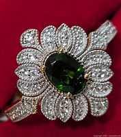 Close-up of the top view showing the oval chrome diopside gemstone center with surrounding decorative clear cubic zirconia in a flower petal pattern.