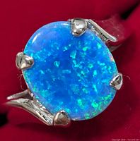 Close-up front view of silver ring with oval opalite stone under clear lighting showing blue and green reflections.