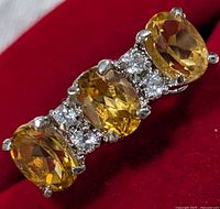 Close-up image of silver ring with three faceted yellow citrine oval stones and several clear cubic zirconia stones between them, showing polished silver prong settings.