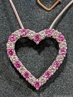 Close-up image of the heart-shaped pendant on a silver snake chain, showing pink tourmaline and white gemstones arranged alternately around the heart.