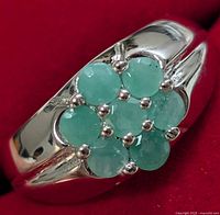 Close-up front view of silver ring showing cluster of six round green emerald gemstones with polished silver band.