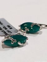 Close-up of one silver earring with marquise shaped green onyx stone and decorative silver prongs
