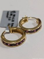 Close-up view of the pair of yellow gold tone silver hoop earrings with inlaid garnet stones, showing stone detail and earring closure.