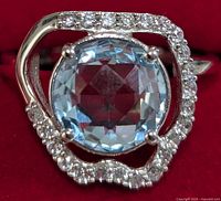 Close-up front view of ring showing round blue topaz center stone and surrounding halo of clear cubic zirconia.