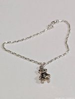 Silver bracelet laid out flat showing full length with attached teddy bear charm, lobster clasp visible.