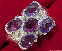Close-up front view of silver ring featuring five faceted oval amethyst stones in a cluster design on red background.