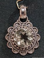 Front view of the silver pendant showing round faceted green amethyst centerpiece surrounded by decorative silver scalloped edging and rope design.