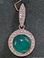 Front view of silver pendant showing round green onyx cabochon surrounded by clear stones and stone-studded bail.