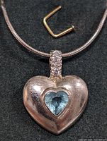 Close-up front view of the sterling silver heart pendant with blue topaz and small clear stones on the bail, showing chain detail.