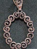 Front view of the oval silver pendant showcasing the detailed spiral and bead pattern on a dark background.