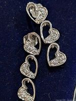 Photo showing the front view of the silver heart-shaped earrings with cubic zirconia stones on a dark background.