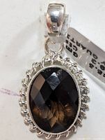 Close-up front view of the oval faceted smokey quartz in silver pendant with scalloped edge design