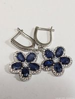 Pair of silver flower earrings with blue sapphire petals and clear stones around them, latch-back clasps visible.