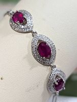 Close-up of three linked marquise-shaped silver sections each with a central oval synthetic ruby surrounded by clear cubic zirconia stones, showing detailed design and setting style.