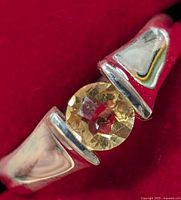 Close-up of silver ring featuring a faceted round citrine gemstone on red background.