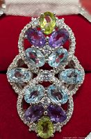 Front view showing the arrangement of the light blue, purple, and yellow-green oval gemstones surrounded by clear accent stones set in sterling silver.