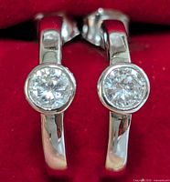 Close-up front view of the pair of silver earrings showing the bezel-set cubic zirconia stones and polished silver hoops against red background.