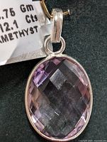 Close-up image of the front of an oval faceted amethyst gemstone pendant in a silver setting, showing the amethyst's purple color, facets, and silver bail attachment.