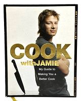 Front cover of Cook With Jamie cookbook showing Jamie Oliver and title in gold letters with a knife illustration