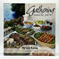 Front hardcover of the 'Gathering Around The Grill' cookbook showing an outdoor food spread and title text.