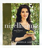 Front cover of Nigellissima cookbook featuring Nigella Lawson holding a bowl with olives, decorative gold and green floral pattern on cover, title showing 'Nigellissima Easy Italian-Inspired Recipes' and author name.