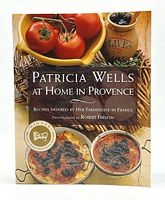 Front cover of the Patricia Wells at Home in Provence cookbook showing fresh tomatoes in a basket, baked dishes, and a jar of olives, along with the book title and author's name.