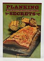Front cover of the 'Planking Secrets' cookbook showing grilled food on wooden planks.