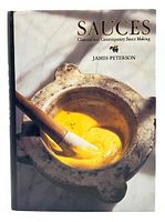 Front cover of the hardcover cookbook showing a mortar with yellow sauce and wooden pestle with title and author name.