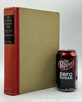 Photo of the hardcover book showing red spine with title and tan cover next to a soda can for scale.