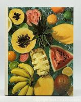 Front cover of the hardcover cookbook showing assorted tropical fruits including papaya, pineapple, watermelon, bananas, mango, and citrus on ice.