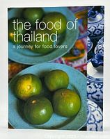 Front view of the cookbook showing the title and cover image featuring green citrus fruits in a blue ceramic bowl and traditional Thai ceramics.