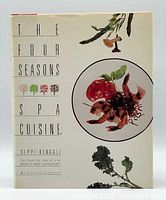 Front cover of the cookbook showing the title, author's name, and food imagery, with cream-colored dust jacket.