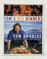 Front cover of the cookbook showing Tom Douglas with seafood dish and dinner party image on top.