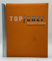 Front cover of the Top Chef Quickfire Cookbook, orange cover with silver text and knife graphic