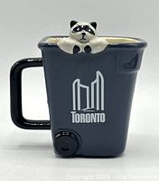Front view showing mug shape, logo and raccoon figurine