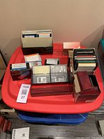 Photo showing multiple 3.5-inch floppy disks in various plastic holders and boxes on a red plastic table.