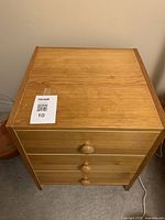 Front view of the light brown wooden night table showing the three drawers with round wooden knobs.