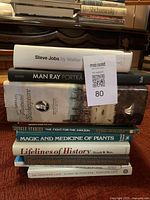 Stack of books including Steve Jobs biography, Man Ray Portraits, Shakespeare, and history titles.