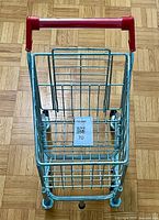 Top view of child’s metal shopping cart showing red handle and wire basket frame.