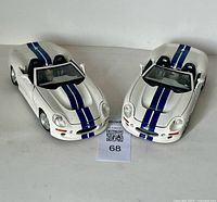 Two white Maisto 1999 Shelby 1/18 scale die cast convertible model cars with blue racing stripes, shown side by side from a front angle.