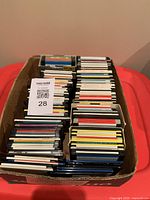Top view of cardboard box filled with approximately 100 mixed brand 3.5-inch floppy disks, some labeled and some blank.