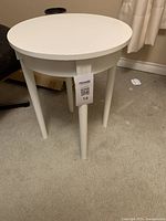 Full view of the white round accent table with four legs on carpeted floor showing overall structure and condition.