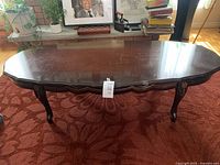 Front and angled side view of dark brown oval wooden coffee table showing cabriole legs and scalloped edge detail.