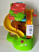 Front and side view of the Weeble Wobble Treehouse toy showing the yellow slide, red roof, green leafy details, and base with flower decorations.