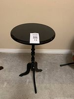 Full view of the black round wooden accent table featuring a tripod leg base and turned pedestal.