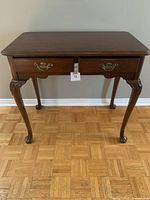 Front view of traditional dark brown glossy wooden table showing two drawers and cabriole legs with carved detailing.