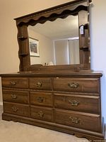 Front view of traditional dark brown wooden dresser with attached mirror and side shelves, showing eight drawers with brass handles.